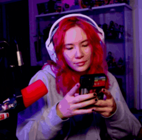 a woman with red hair and headphones is looking at her phone