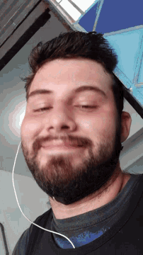 a man with a beard has his eyes closed and his ear buds around his neck