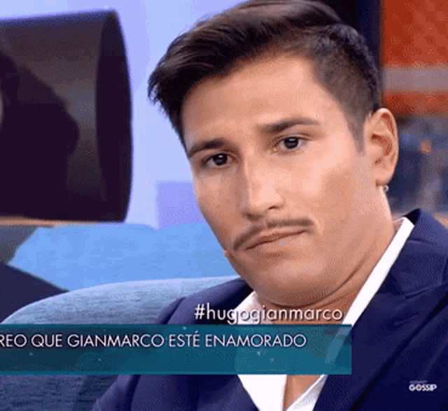 a man with a mustache is sitting in front of a sign that says #hugoglianmarco