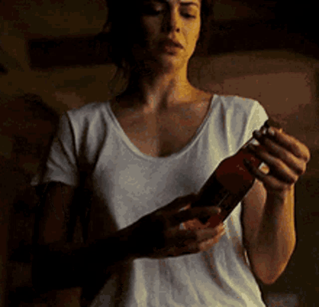 a woman in a white shirt is holding a bottle in her hands