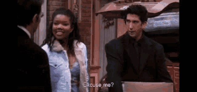a man in a suit is standing next to a woman in a blue dress and talking to her .