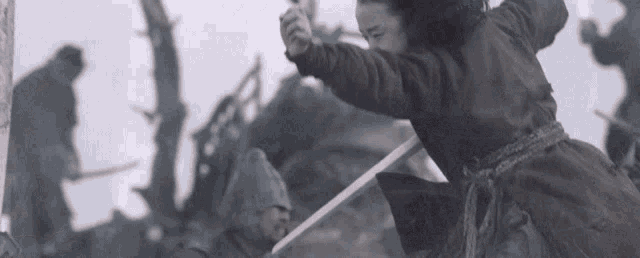 a woman in a red coat is holding a sword in a battle scene