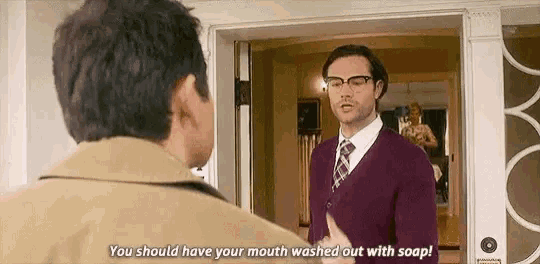 a man in a purple sweater and tie is talking to another man in a tan jacket .