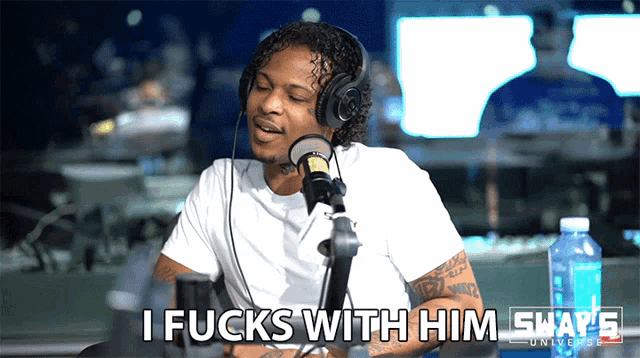a man wearing headphones is sitting in front of a microphone and says i fucks with him