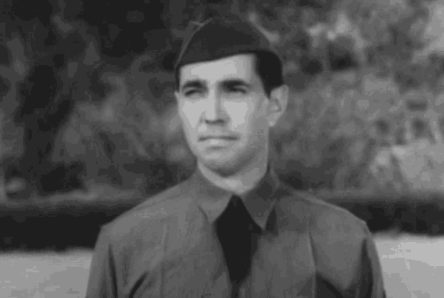 a black and white photo of a man in a military uniform with a hat on .