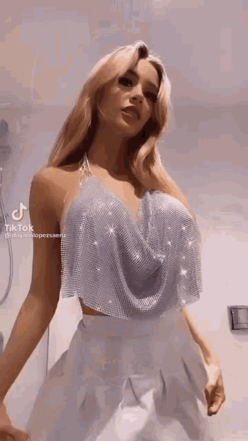 a woman wearing a silver top and white pants is standing in front of a shower .