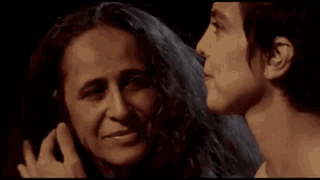 two women are standing next to each other in a dark room and one of them is touching the other 's hair .