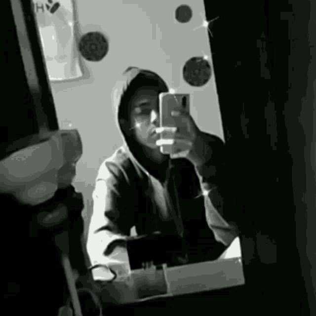 a man in a hoodie is taking a selfie in the mirror