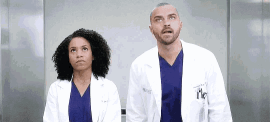 a man and a woman in lab coats and scrubs are standing next to each other in an elevator .