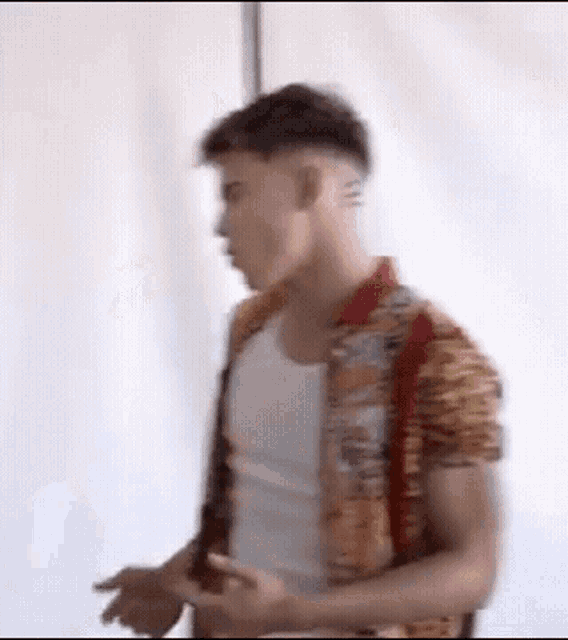 a man wearing a colorful shirt and a white tank top is standing in front of a white wall .