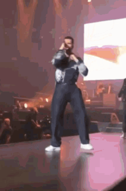 a man dancing on a stage with a large screen behind him
