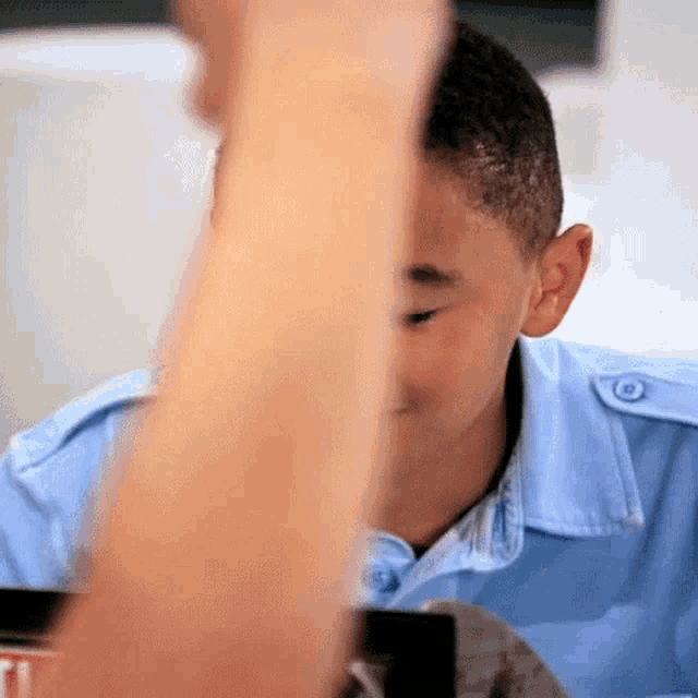 a boy in a blue shirt is looking at a cell phone