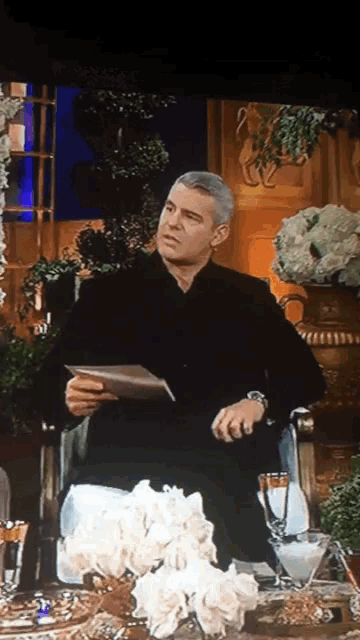 a man in a black suit is sitting in a chair holding a piece of paper