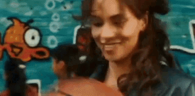 a woman is smiling in front of a painting of a fish on a wall .