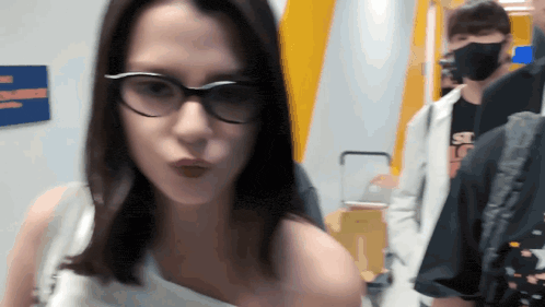 a woman wearing glasses stands in front of a man wearing a mask