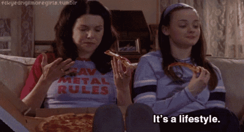 two girls are sitting on a couch eating pizza and one has a shirt that says " raw metal rules "
