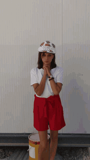 a woman wearing a white shirt and red shorts is standing in front of a white wall