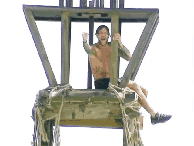 a man without a shirt is sitting on a wooden box with his arms in the air