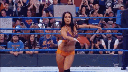 a woman is dancing in a wrestling ring while a crowd watches .
