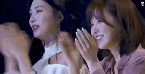 a couple of women are sitting next to each other and clapping their hands .