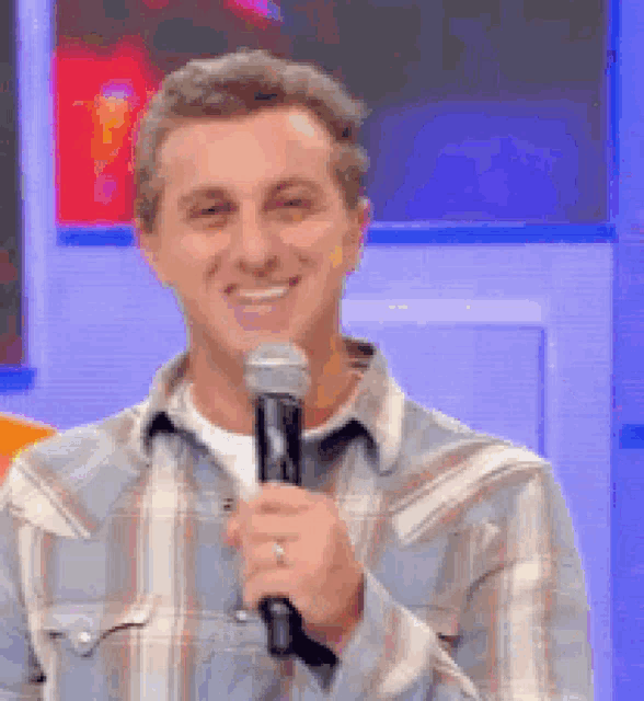 a man in a plaid shirt is smiling while holding a microphone .