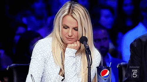 britney spears is sitting in front of a microphone with a pepsi cup in her hand .