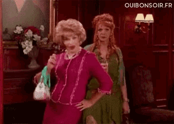 a woman in a pink dress is standing next to another woman in a green dress holding a pink purse .