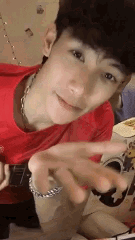 a young man wearing a red shirt and a silver chain around his neck is playing a guitar .