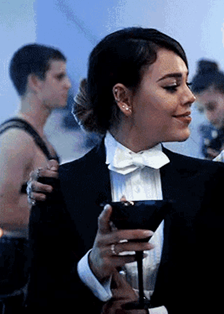 a woman in a tuxedo is holding a glass of wine