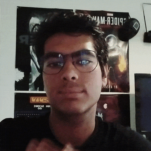 a young man wearing glasses stands in front of a poster that says spider-man