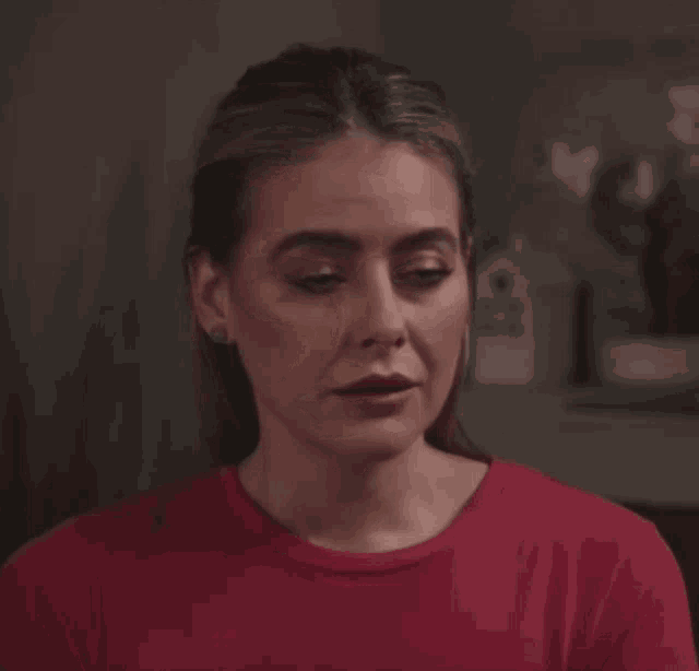 a woman wearing a red shirt and earrings looks at the camera