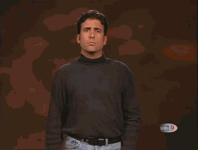 a man wearing a black turtleneck sweater is making a sign