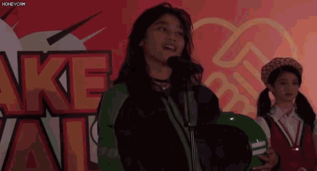 a girl singing into a microphone in front of a sign that says ake all