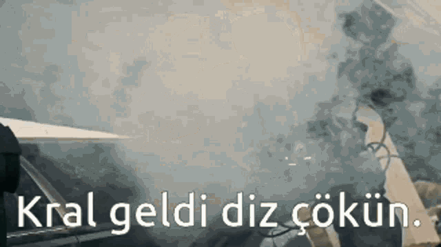 a man is smoking a cigarette in a car with the words kral geldi diz cokun