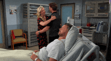 a man is laying in a hospital bed with a woman and a man standing around him