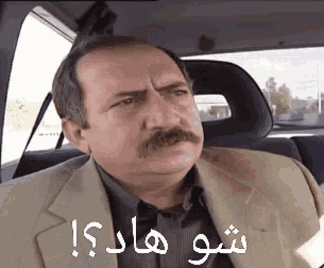 a man with a mustache is sitting in the back seat of a car with arabic writing