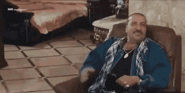 a man in a blue jacket is sitting in a chair and making a funny face .