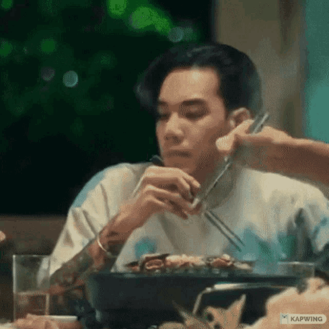a man is sitting at a table eating food with chopsticks and a bowl of food .