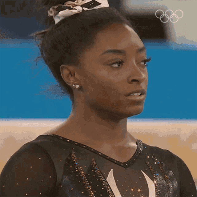 a close up of a female gymnast 's face with the olympic rings behind her