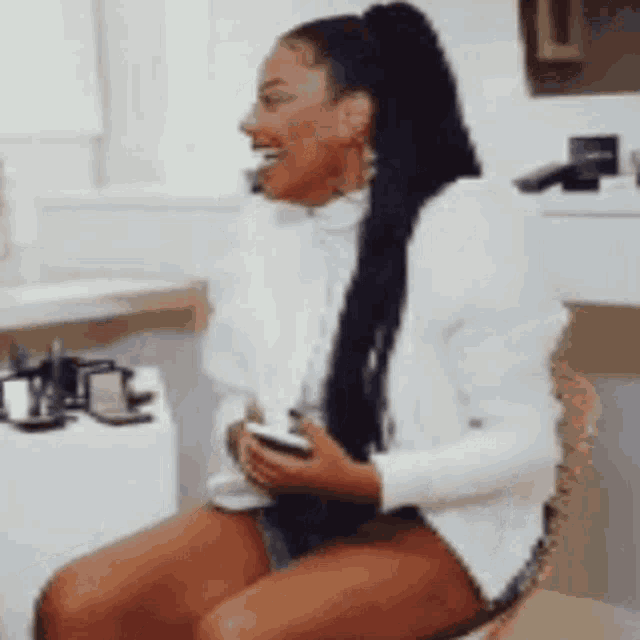 a woman is sitting on a chair with her legs crossed and holding a cell phone .