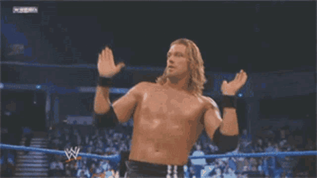 a shirtless wrestler is standing in a wrestling ring with his hands up
