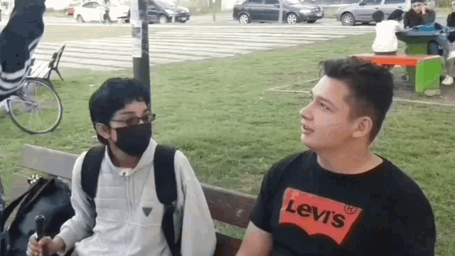 a man wearing a levi 's shirt sits next to another man wearing a black mask