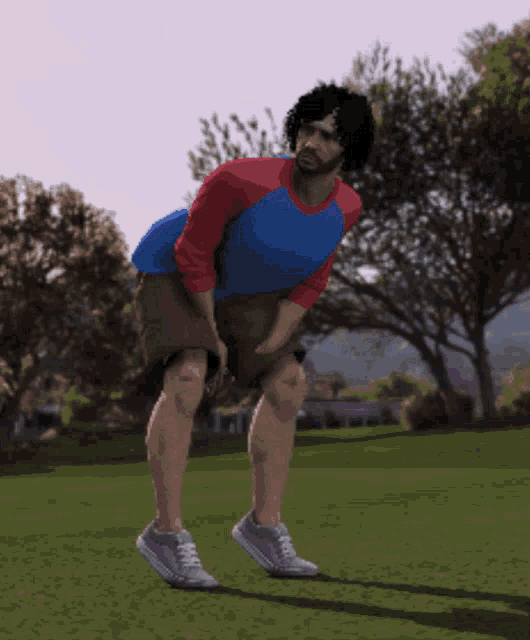 a man in a blue and red shirt is kneeling down on a grassy field