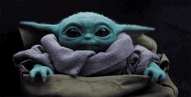 a baby yoda is wrapped in a brown blanket