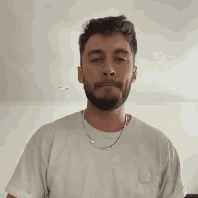 a man with a beard is wearing a white shirt and a silver chain around his neck