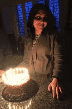 a woman stands in front of a birthday cake with candles lit up