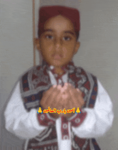 a boy wearing a red hat and a white shirt with arabic writing