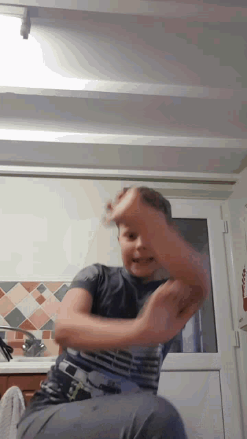 a young boy in a gray shirt is sitting in a kitchen