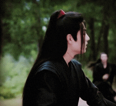 a man with long hair is wearing a black shirt and has a red ribbon in his hair .