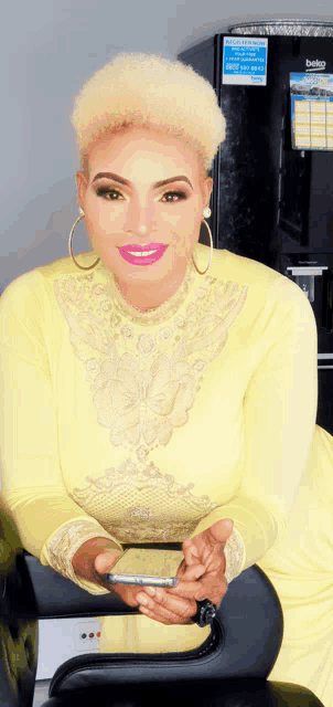 a woman in a yellow dress is holding a cell phone in front of a beko refrigerator